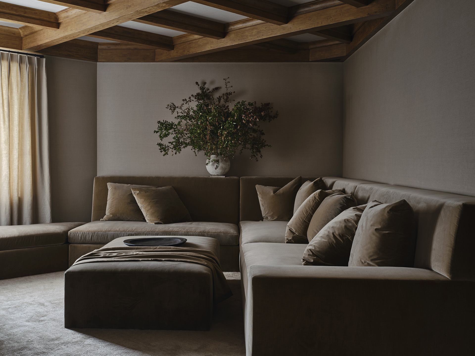 Warm sectional and upholstered ottoman beneath a timber ceiling